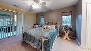 Une chambre à coucher avec un lit, un ventilateur de plafond, une fenêtre et une petite table avec une lampe.