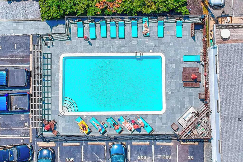 An aerial view of a rooftop swimming pool with lounge chairs, a diving board, and a parking area.