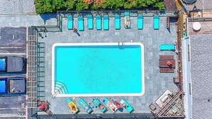 An aerial view of a rooftop swimming pool with lounge chairs, a diving board, and a parking area. - Upscale condo in heart of Dewey with pool & AC - walk to beach, bay & hot spots (Dewey Beach)