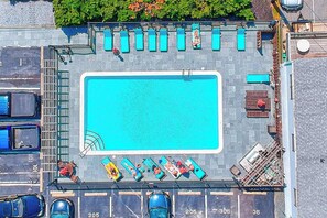 Vue aérienne d’une piscine sur le toit, avec des chaises longues, un plongeoir et un espace de stationnement.