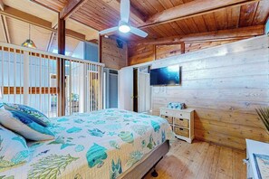 Un dormitorio con paneles de madera, una cama, un ventilador de techo, un televisor y un aparador blanco.