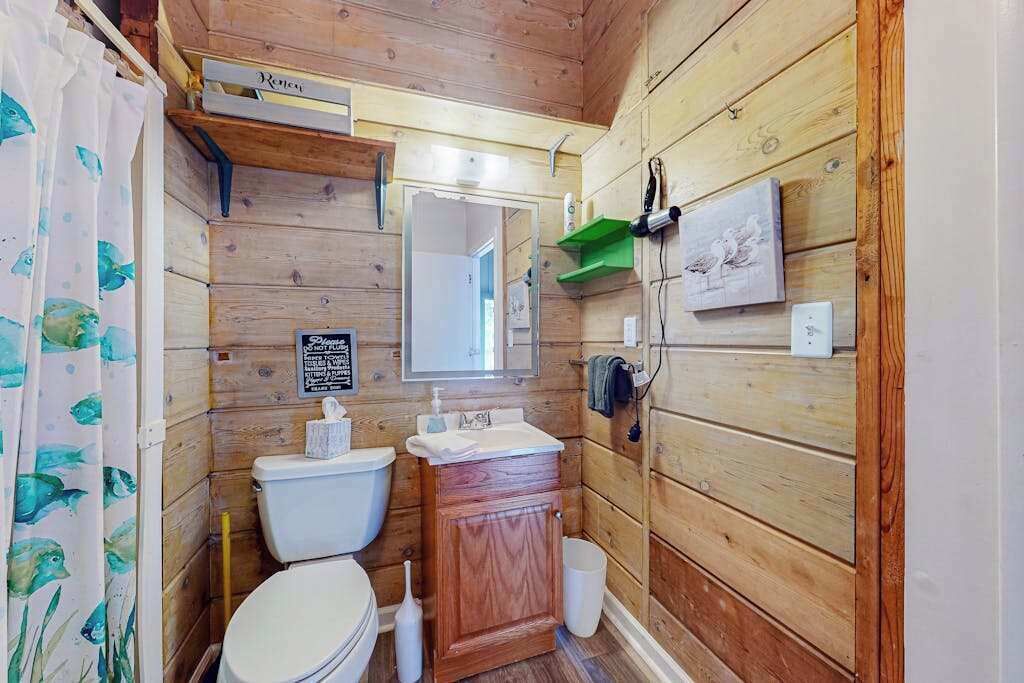 Un baño con paneles de madera, un inodoro, lavamanos y espejo.