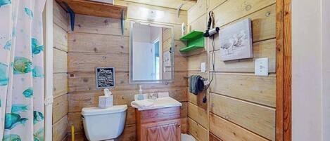 Un baño con paneles de madera, un inodoro, lavamanos y espejo.