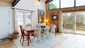 A dining area with a wooden table and chairs, a colorful abstract painting, and a view through large windows.