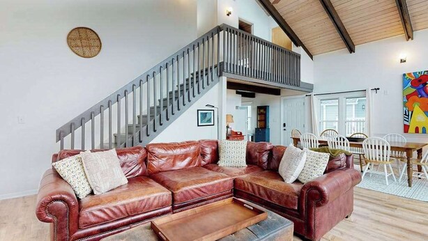 A spacious living area with a leather sectional sofa, a wooden coffee table, a staircase, and a dining area with white chairs.