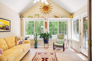 A sunroom with a yellow couch, green chair, potted plants, and a large window with a view of trees. - Lovely dog-friendly home with tennis, fast WiFi, deck, grill & W/D (Lewes)