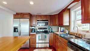 A modern kitchen with wooden cabinets, stainless steel appliances, a large island, and a window providing natural light. - Town of Lewes condo steps from the park w/Tennis, Pickleball & Basketball (Lewes)