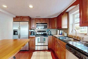 A modern kitchen with wooden cabinets, stainless steel appliances, a large island, and a window providing natural light. - Town of Lewes condo steps from the park w/Tennis, Pickleball & Basketball (Lewes)