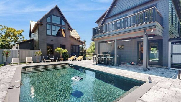 Ein modernes, zweistöckiges Haus mit Schwimmbad, Sitzgelegenheiten im Freien und einer überdachten Terrasse.