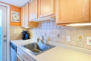 A kitchen with wooden cabinets, a stainless steel sink, a coffee maker, and a dishwasher. - 2nd-floor Sunspot condo steps from beach with balcony, outdoor shower, W/D, & AC (Dewey Beach)