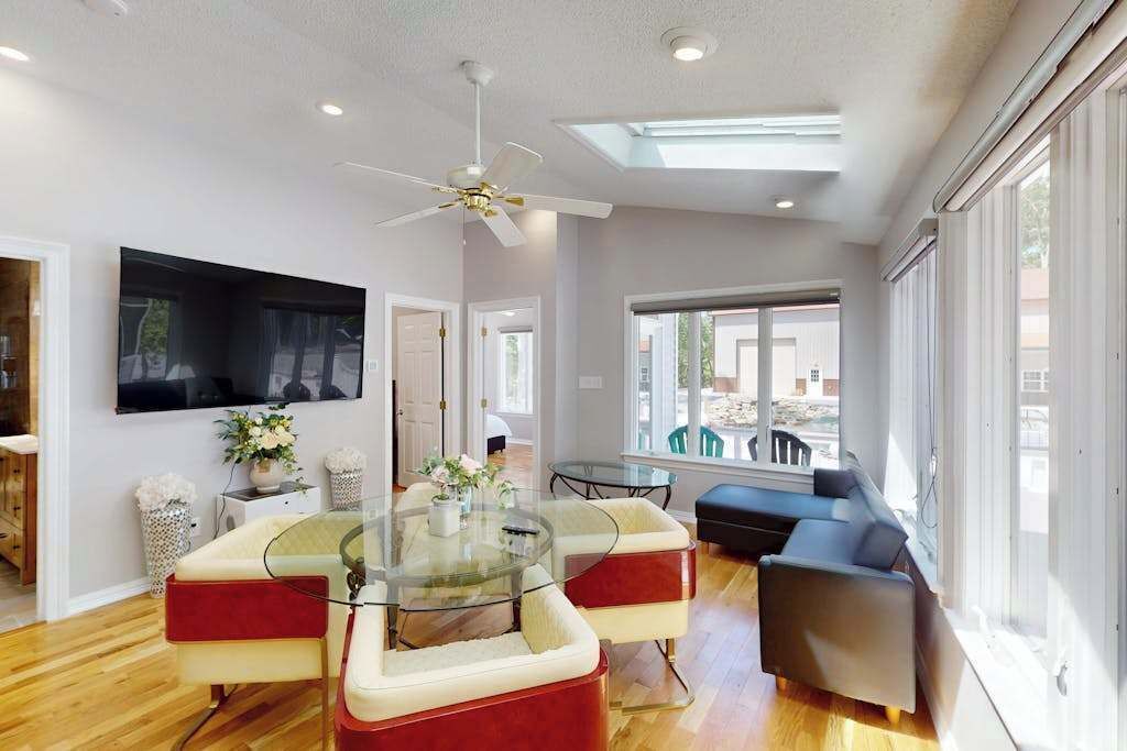 Un salon moderne avec une table basse en verre, des fauteuils rembourrés de couleur rouge, un canapé, un ventilateur de plafond et un téléviseur fixé au mur.