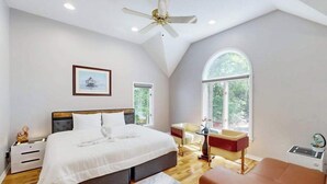 Une chambre à coucher avec un grand lit, un bureau, une chaise, un canapé et un ventilateur de plafond.