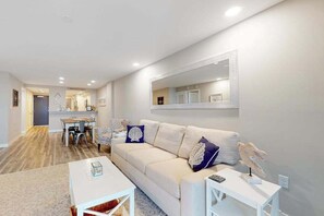 A living room with a sofa, coffee table, and a dining area with chairs and a table. - Sea Colony 6th floor condo w/ elevator, pool, and shared sauna (Bethany Beach)