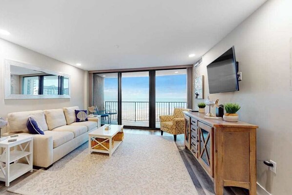A modern living room with a sofa, coffee table, and a TV mounted on the wall. - Sea Colony 6th floor condo w/ elevator, pool, and shared sauna (Bethany Beach)