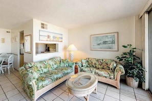 A living room with two floral sofas, a round coffee table, a lamp, a painting, and a potted plant. - Sea Colony 6th floor condo w/ shared gym, basketball court - partial ocean view (Bethany Beach)