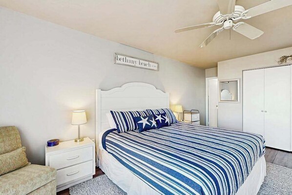 A bedroom with a bed, nightstands, a ceiling fan, a wardrobe, and a wall sign. - Sea Colony 1st floor condo w/ gym, tennis court, and balcony - ocean view (Bethany Beach)