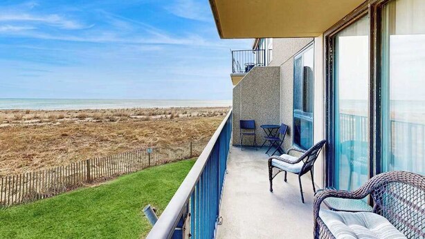 Ein Balkon mit Blick auf den Strand, ein kleiner Tisch und Stühle sowie eine Glastür zum Innenbereich.
