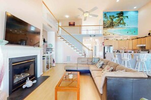 A spacious living room with a fireplace, a large TV, a staircase, a kitchen area, and a dining space. - Swann Cove house with free WiFi and pool (Selbyville)