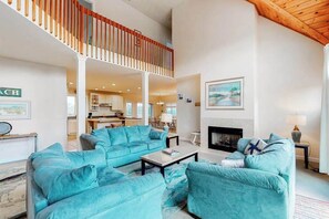 A spacious living room with a high ceiling, a staircase, and a fireplace. - Quillens Point home w/ 5 decks, screened porch, grill & shared tennis - dogs OK (Ocean View)