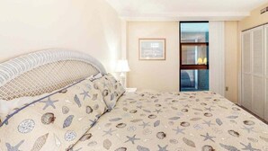 A bedroom with a bed, a nightstand, a lamp, a framed picture on the wall, and a sliding door leading to a bathroom. - Sea Colony 7th floor condo with ocean veiw, pool, basketball court &  gym (Bethany Beach)
