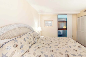 A bedroom with a bed, a nightstand, a lamp, a framed picture on the wall, and a sliding door leading to a bathroom. - Sea Colony 7th floor condo with ocean veiw, pool, basketball court &  gym (Bethany Beach)