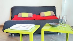Ein modernes Zimmer mit einer Couch, zwei gleichfarbigen gelben Tischen und einer Glasvase auf einem Tisch.