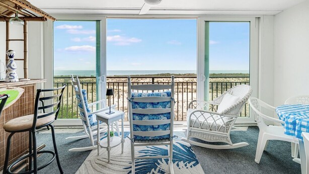 Un balcone con vista sull'oceano, mobili in vimini e una ventola a soffitto.