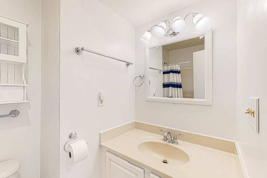 A bathroom with a sink, mirror, towel rack, and toilet paper.