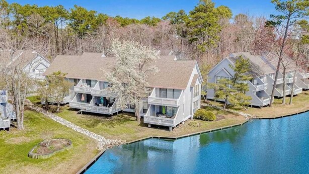 A lakeside property with multiple houses, each featuring a balcony and a front porch. - Sea Colony Tennis 1st floor condo w/ tennis court, basketball court, and pool (Bethany Beach)