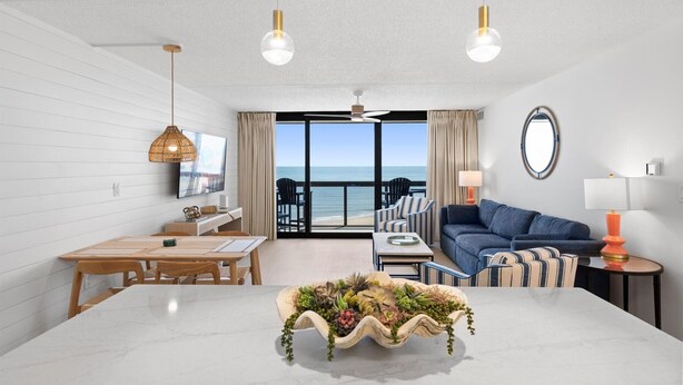 A modern room with a dining table, sofa, and a view of the sea. - Golden Sands 1018 by Seaside Vacations & Sales (Ocean City)