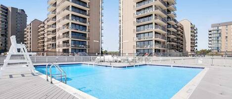 A swimming pool with a wooden deck, surrounded by multi-story residential buildings.