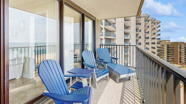 A balcony with two Adirondack chairs and a glass door leading to an indoor area. - Sea Colony condo in oceanside complex with washer/dryer, shared hot tub & pool (Bethany Beach)