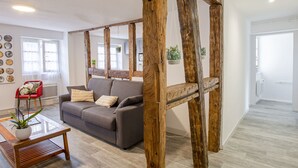 Una sala de estar con estructura de vigas de madera, un sofá gris, una silla roja y una mesa de centro de vidrio con una planta.