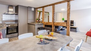 Una cocina moderna con electrodomésticos de acero inoxidable, un comedor con mesa dispuesta para el desayuno y una sala de estar con sofá y televisor.