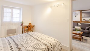 Un dormitorio con cama, escritorio y silla. Se ve una ventana con cortinas de encaje y una planta en el escritorio.