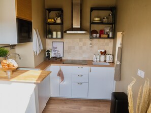 A compact kitchen with white cabinets, a wooden countertop, a black range hood, and a shelf with kitchen items. - Apartment in Cannes: rooftop and sky views (Cannes)
