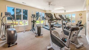 Una palestra con diverse attrezzature per esercizi, ampie finestre e una ventola a soffitto.