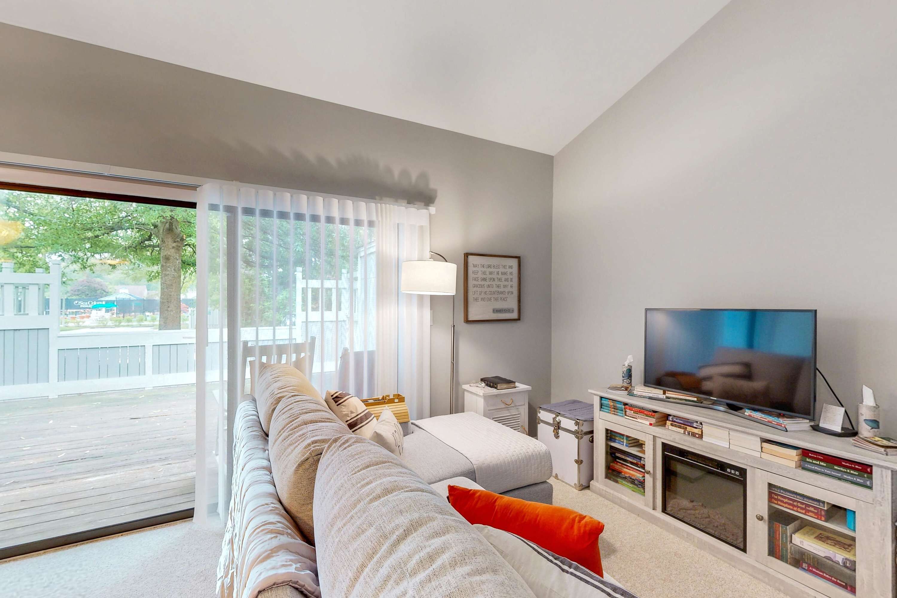 A living room with a sofa, television, bookshelves, and a window with curtains.