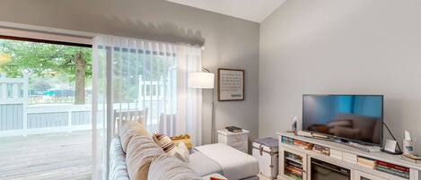 A living room with a sofa, television, bookshelves, and a window with curtains.