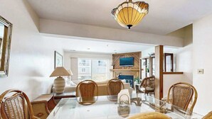 A dining area with a glass table and wicker chairs, a television above the fireplace, and a large window. - Indian Harbor Villas home close to the beach with private washer/dryer & WiFi (Bethany Beach)