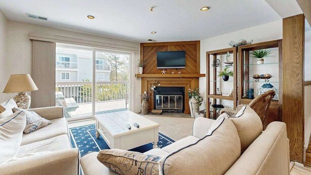 A living room with a fireplace, a television, and a balcony with a view of buildings. - Indian Harbor Villas home close to the beach with private washer/dryer & WiFi (Bethany Beach)