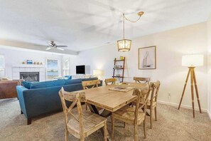 A dining area with a wooden table and chairs, a ceiling fan, and a chandelier. - Bay view condo with screened porch, central AC, on-site golf and shared pool (Ocean View)