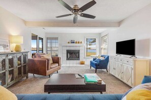 A living room with a fireplace, a ceiling fan, a television, and a view of the outdoors. - Bay view condo with screened porch, central AC, on-site golf and shared pool (Ocean View)