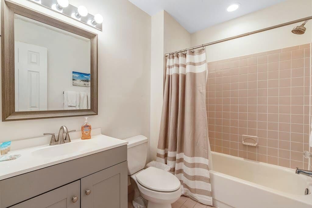 A bathroom with a sink, toilet, mirror, and shower.