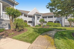 A residential building with a covered patio, a lawn, and a pathway. - Bay view condo with screened porch, central AC, on-site golf and shared pool (Ocean View)