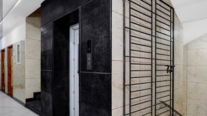 A hallway with a black elevator door, a metal security gate, and marble flooring. - Saver Double Royapettah Clock Tower RKH (Chennai)