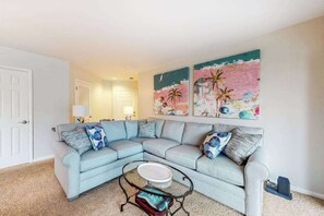 A living room with a light blue sectional sofa, a glass coffee table, and two wall-mounted paintings. - Sea Colony Condo with Pools, Tennis, Beach Access, WiFi, Central AC, and W/D (Bethany Beach)