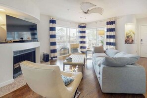 A living room with a fireplace, a sofa, a chair, and a dining table. - Sea Colony Waterfront Condo w/Deck, Private Beach, Shared Pools, Hot Tub, Tennis (Bethany Beach)