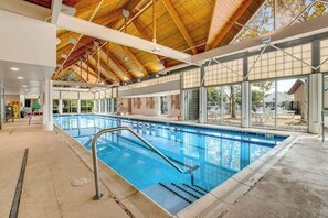 An indoor swimming pool with a wooden ceiling, large windows, and a concrete floor. - Bear Trap Dunes condo with screened porch, deck, pools, saunas & beach shuttle (Ocean View)
