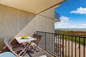 Een balkon met een tafel en stoelen, een uitzicht op het strand en een heldere lucht.